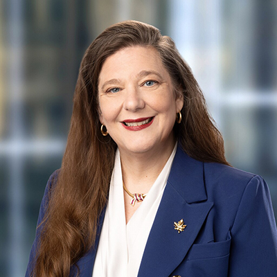 DM of Bank of Canada. She has long auburn hair, a blue jacket and a white blouse. She is smiling.